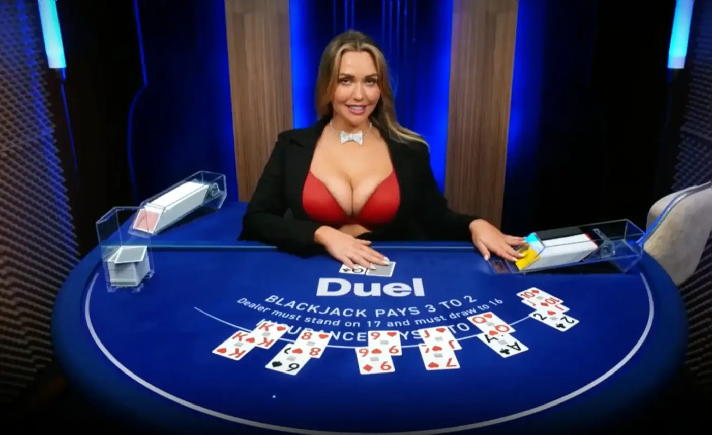 Guest host in a black blazer behind the blue felt at the Duel Blackjack Live table, Duel branding visible while cards are dealt mid-stream